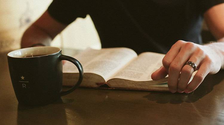 a seated man doing devotions at a table with coffee