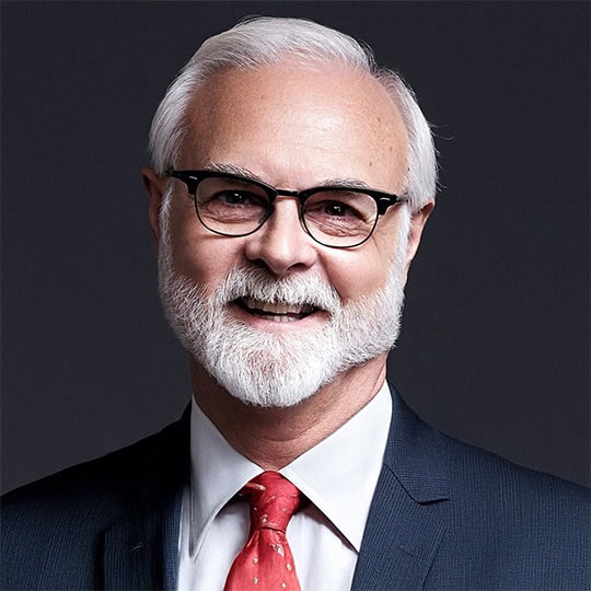 white-haired man in a suite with a red tie and glasses