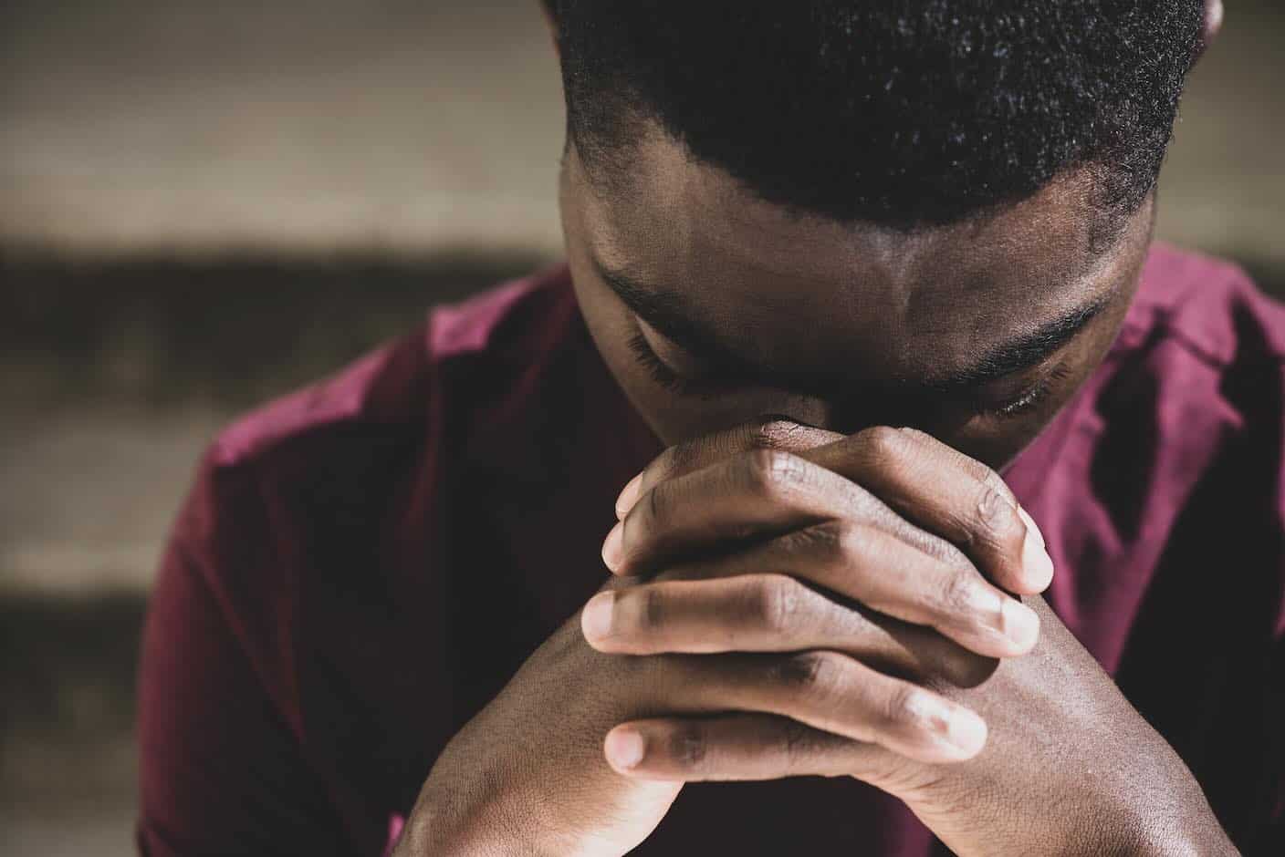 African man praying with face in clasped hands