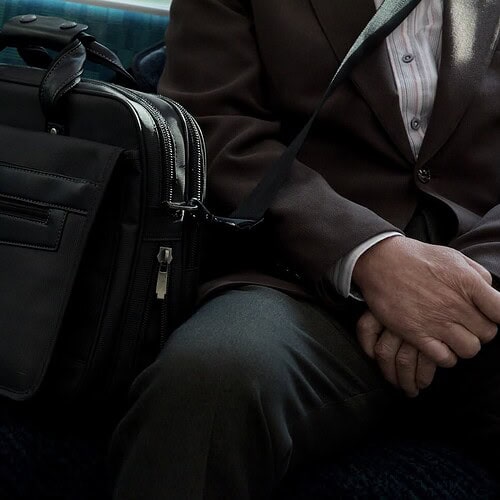 a train seat with a briefcase next to a man's lap to signify a bivocational pastor