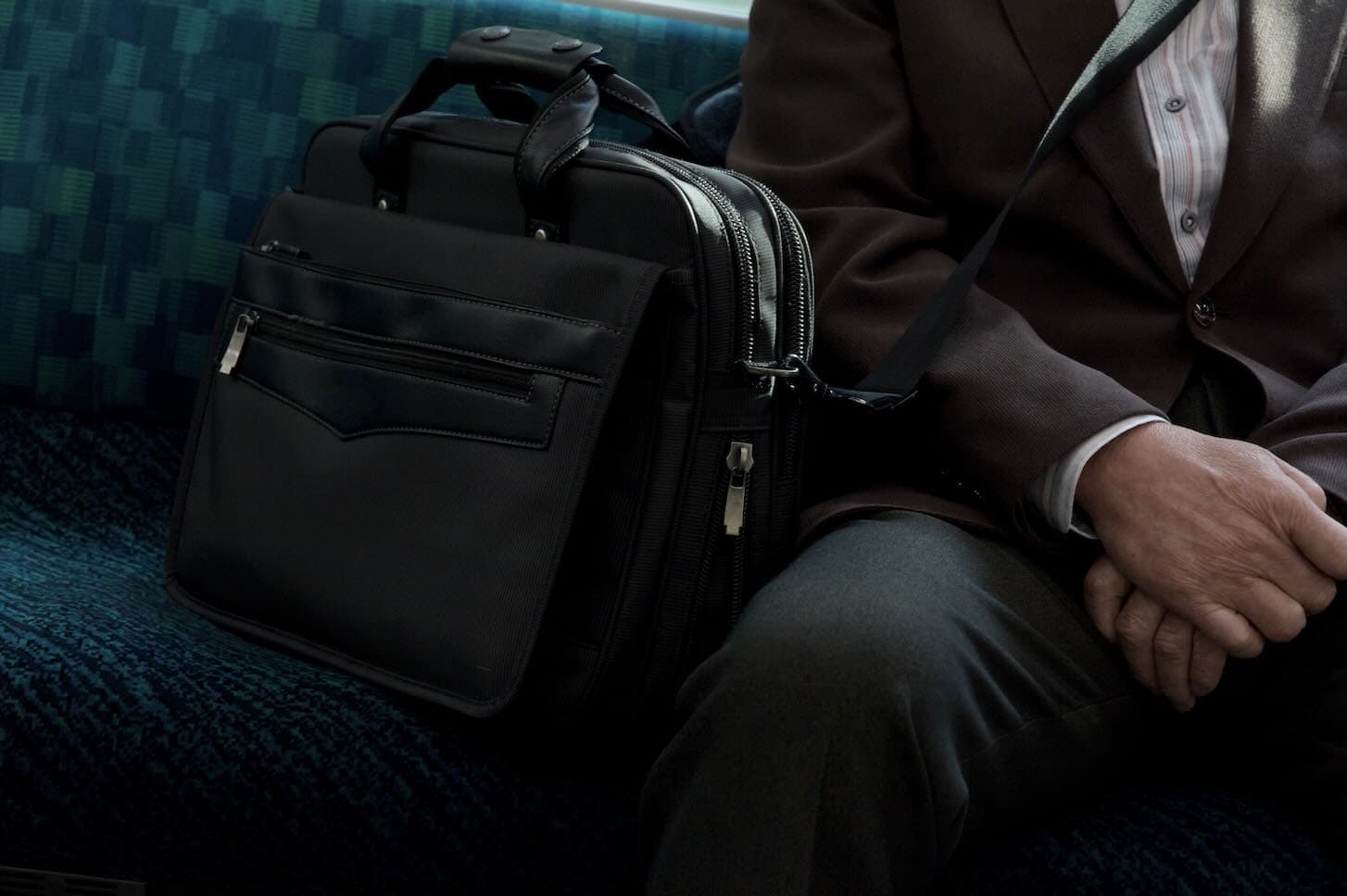 a train seat with a briefcase next to a man's lap to signify a bivocational pastor