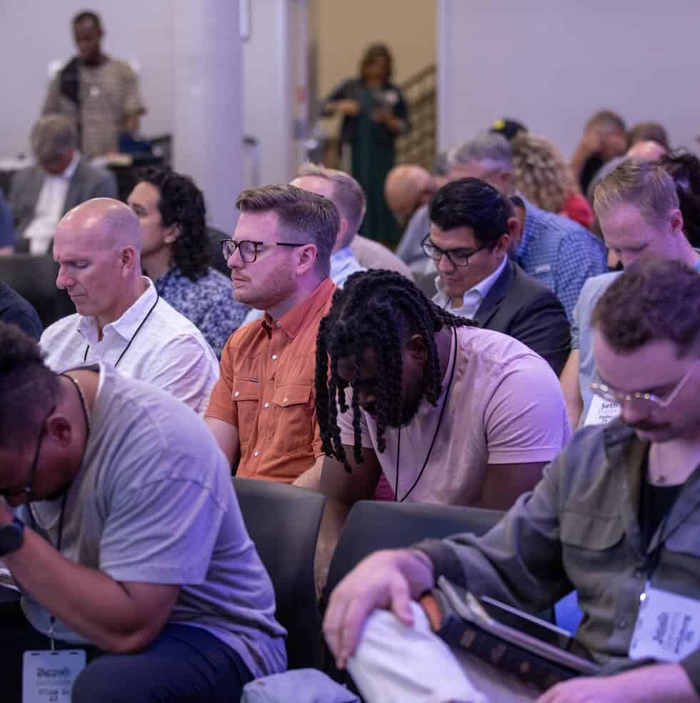 a section of a full room with seated people, from diverse backgrounds, praying