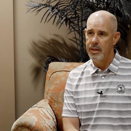 bald man sitting on a chair in front of a plant
