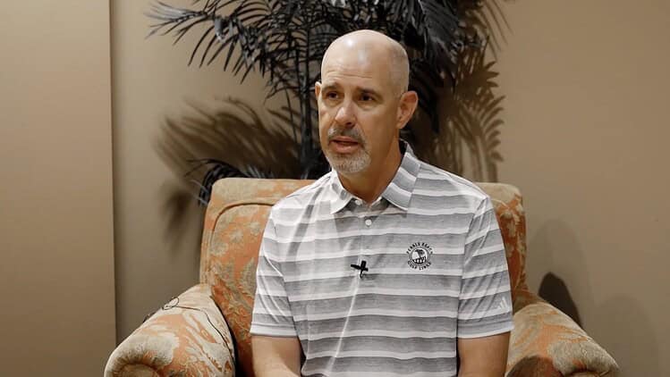 bald man sitting on a chair in front of a plant