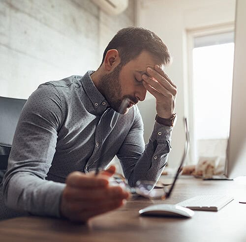 Man with glasses in hand and fingers on forehead feeling fatigue and pastoral burnout
