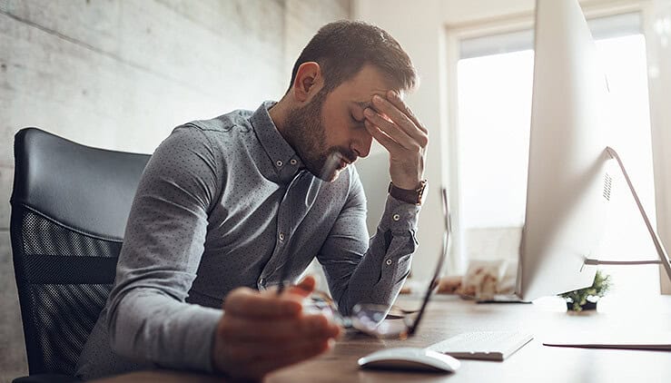 Man with glasses in hand and fingers on forehead feeling fatigue and pastoral burnout
