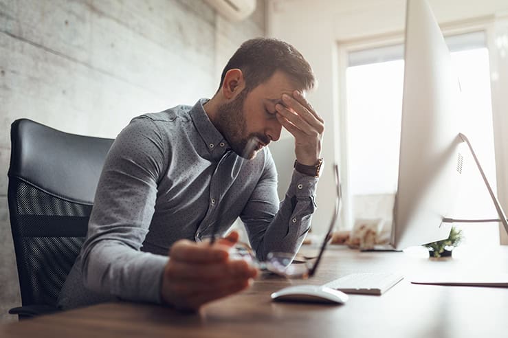 Man with glasses in hand and fingers on forehead feeling fatigue and pastoral burnout