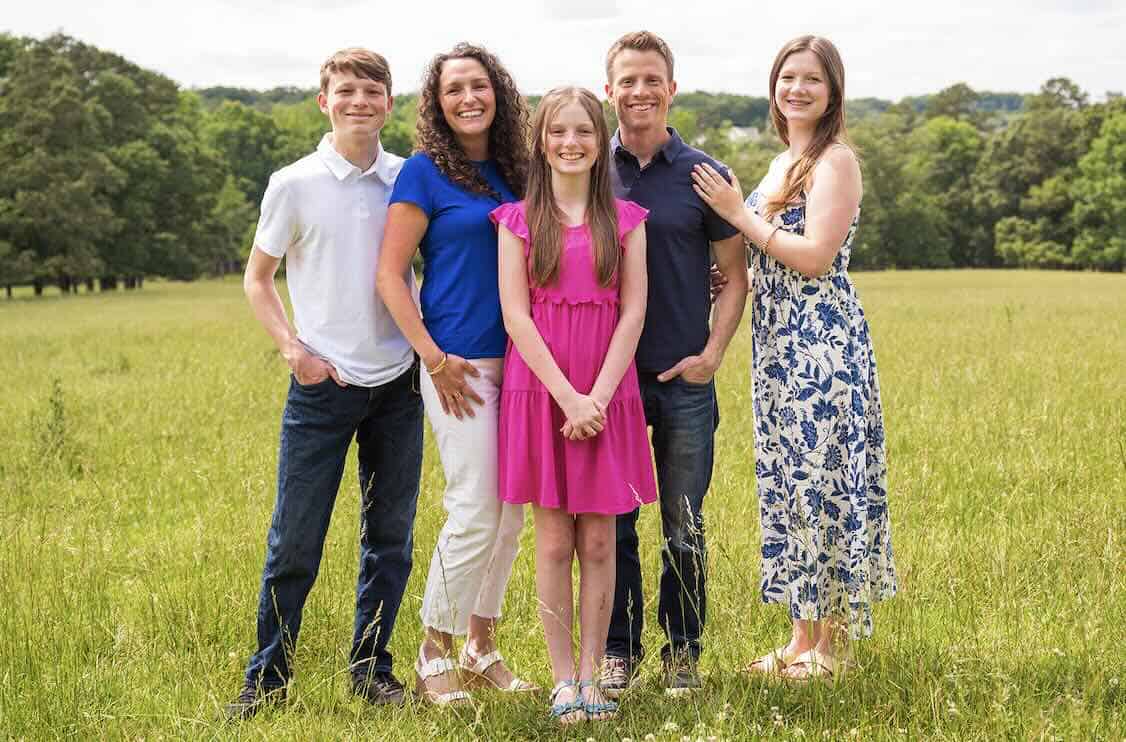 a family, dad, mom, and three kids, standing in a meadow