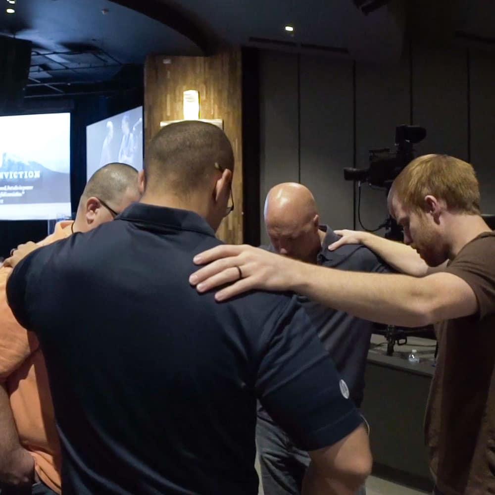 Four pastors stand in a circle and pray together.